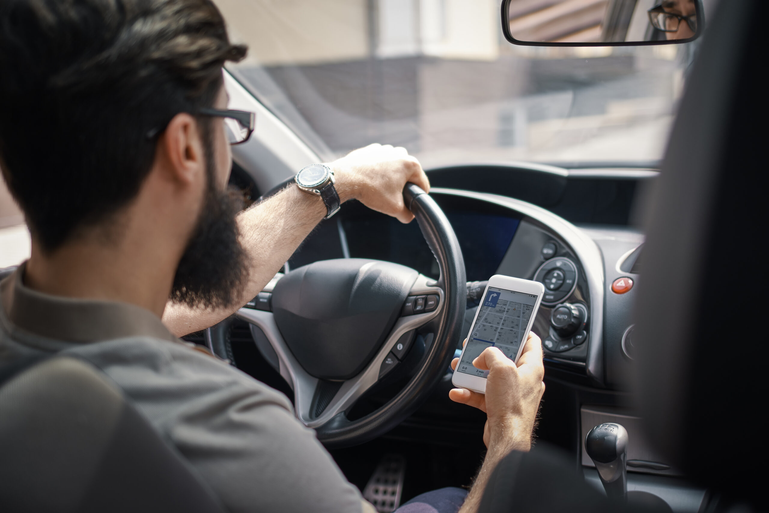 Man searching destination direction or address on gps or navigator application via mobile smartphone inside a car while driving car - back view. Technology, distraction and driving concept